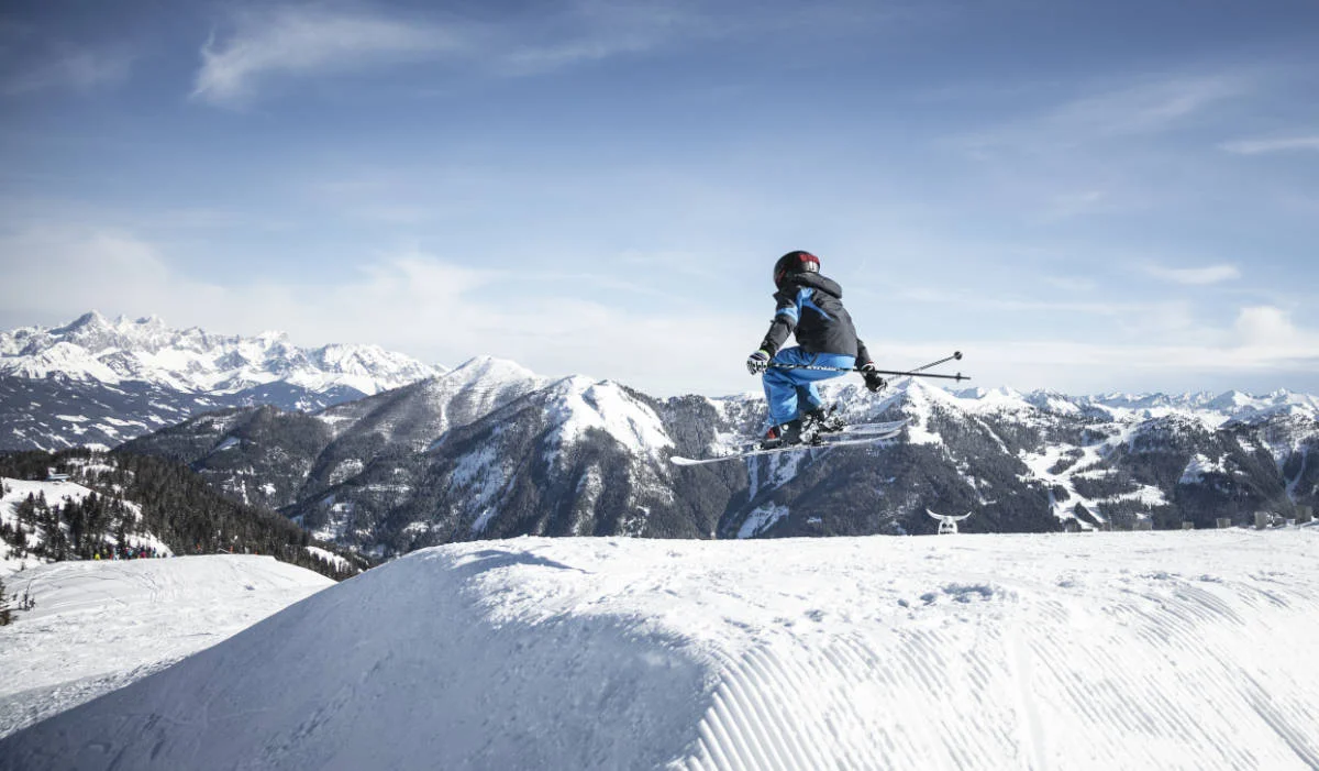 Kinder beim Skisprung – Ski-Leasing & Skitauschsystem Frankfurt Kind springt mit Ski über eine Schneekante vor alpiner Bergkulisse – Bild für Ski-Leasing für Kinder in Frankfurt