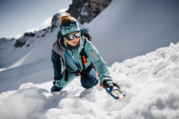 Wintersportlerin sucht im Tiefschnee nach einer Verschütteten – professionelle Lawinenausrüstung für maximale Ski Sicherheit.
