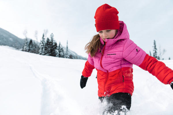 Kind läuft durch tiefen Schnee in funktionaler Skijacke – hochwertige Ski Bekleidung für Kinder.