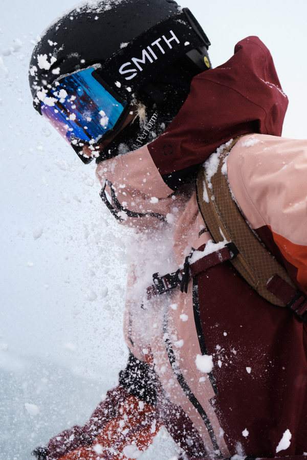 Wintersportlerin mit hochwertiger Skibrille und Skihelm fährt durch Schneespray – wichtige Ski Sicherheitsausrüstung für alpine Bedingungen
